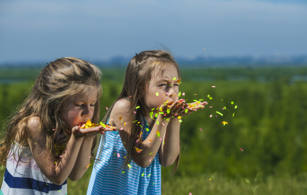 Две маленькие девочки сдувают конфетти  с рук