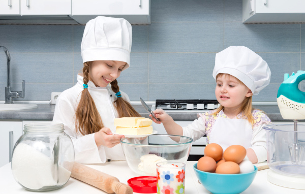 Две маленькие девочки в костюмах повара готовят на кухне
