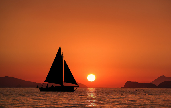 Парусная лодка в море на закате солнца