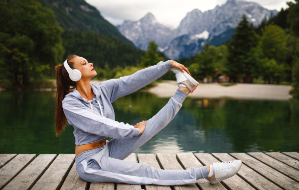 Girl in headphones doing gymnastics on a bridge by the lake