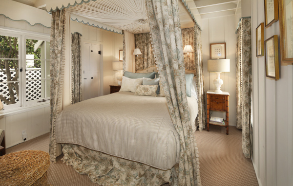 Высокая кровать с занавесками в спальной комнате в пастельных тонах 