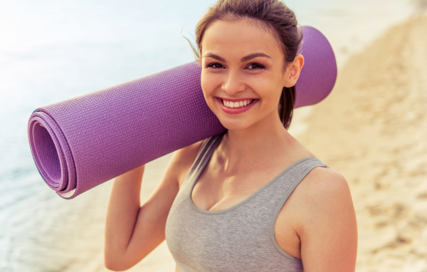 Спортивная девушка с ковриком для йоги на пляже