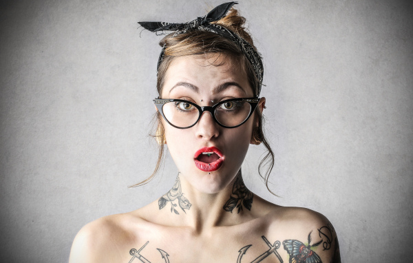 Удивленная девушка в очках с татуировками на теле