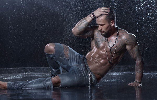 Мужчина в татуировках лежит на земле под дождем