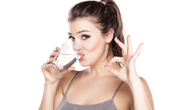 Молодая спортивная девушка пьет воду из стакана