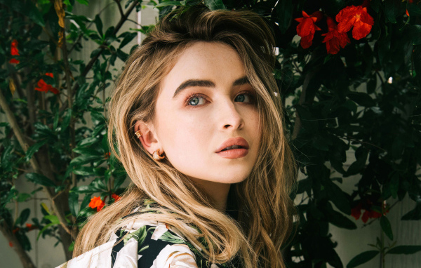 Молодая красивая актриса Сабрина Карпентер у красных цветов