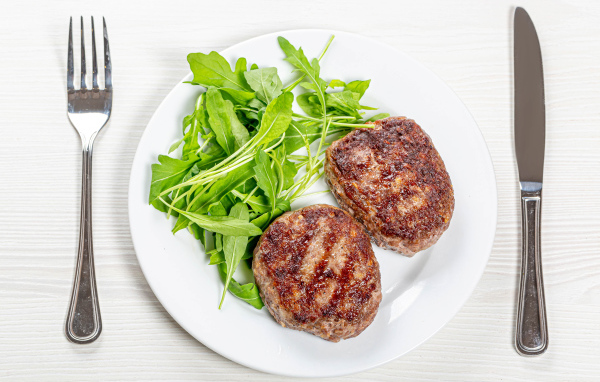 Две котлеты на тарелке с зеленью рукколы 