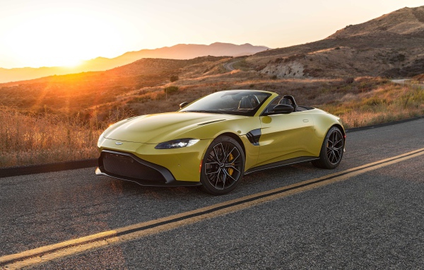 Желтый кабриолет  Aston Martin Vantage Roadster, 2021 года на трассе на рассвете