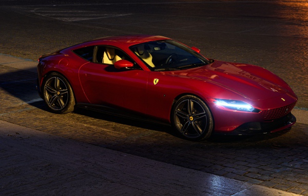 Красный автомобиль Ferrari Roma 2020 года с включенными фарами вечером