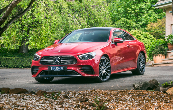 Красный автомобиль Mercedes-Benz E 300 AMG, 2020 года у дома осенью