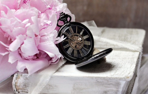Черные карманные часы с книгой и цветами на столе 