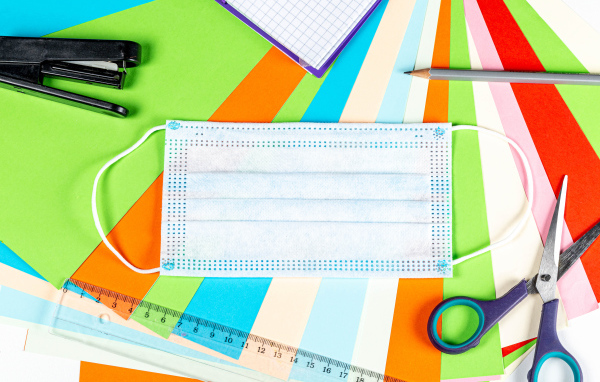 Маска от коронавируса лежит на цветной бумаге с канцелярскими предметами