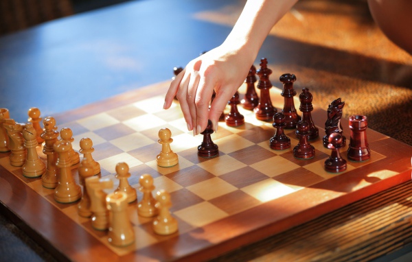 Женская рука переставляет шахматы на доске 