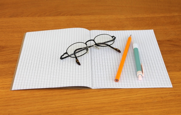 Тетрадь, ручка, карандаш и очки лежат на парте