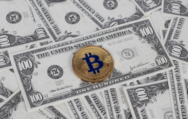 Монета Биткоин лежит на стодолларовых купюрах