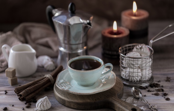 Чашка эспрессо на столе с корицей, зефиром и зажженными свечами