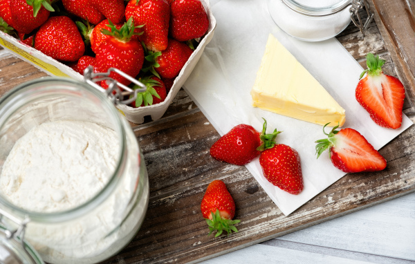 Кусок масла на столе с клубникой и мукой 