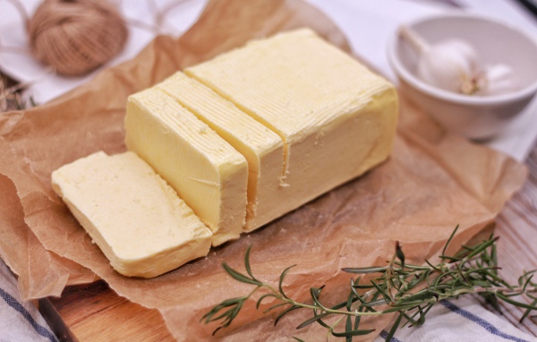 Кусок свежего сливочного масла на столе с розмарином и чесноком