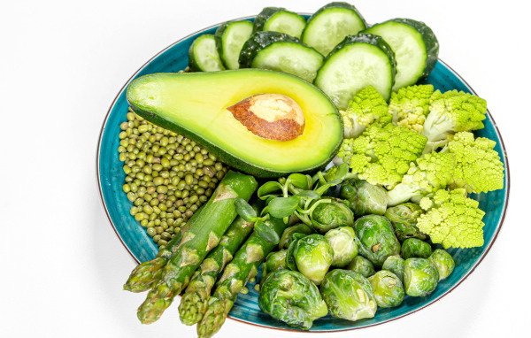 Авокадо, капуста, огурцы и спаржа на тарелке на белом фоне