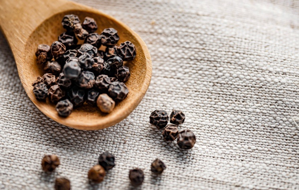 Черный перец горошком на деревянной ложке