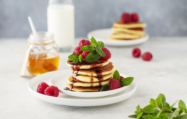 Румяные оладьи на тарелке с малиной и мятой 