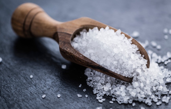 Крупная белая соль в лопатке на столе 