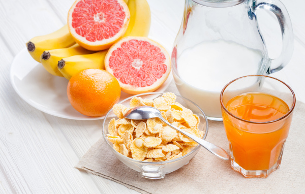 Кукурузные хлопья на столе с молоком, соком и свежими фруктами на завтрак