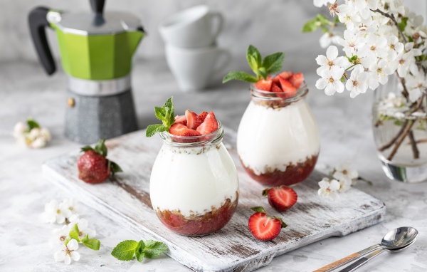 Десерт с йогуртом в банке с клубникой на столе цветами вишни 