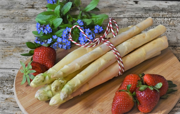 Fresh asparagus on the table with strawberries and forget-me-not flowers