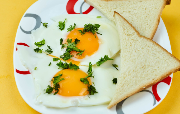 Яичница глазунья с зеленью на тарелке с хлебом 