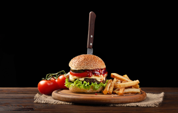 Гамбургер с ножом на столе с помидорами и картофелем фри 