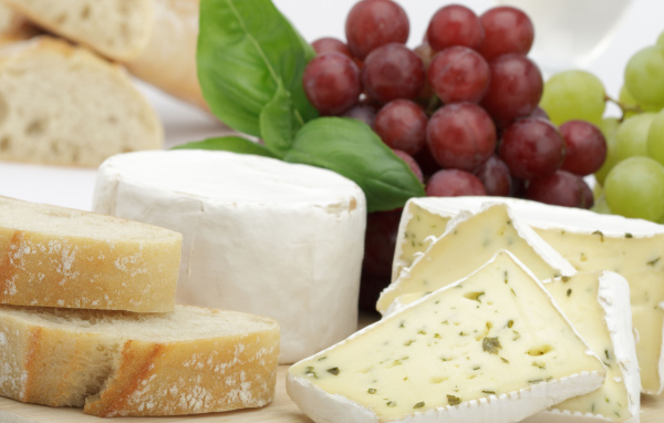 Твердый сыр на столе с батоном и виноградом