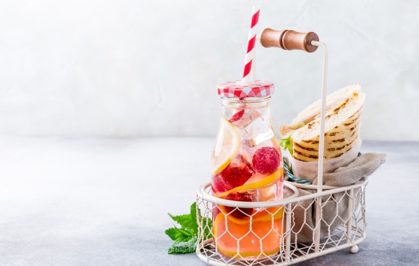 Банка с лимонадом в маленькой корзине с сэндвичем 