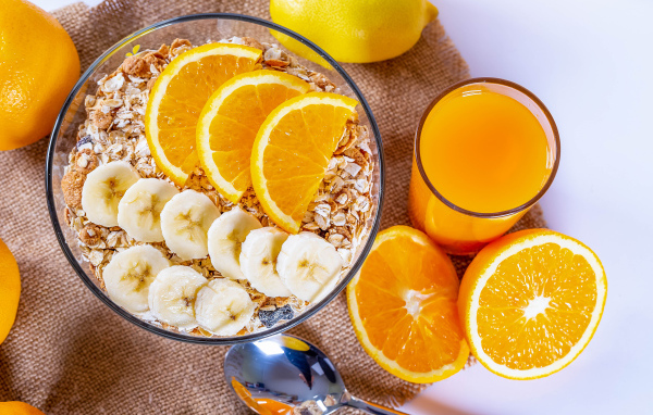 Овсяные хлопья в тарелке с кусочками банана и апельсина на столе с соком