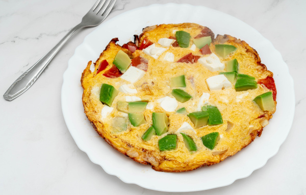 Омлет с авокадо и кусочками помидора на белой тарелке 