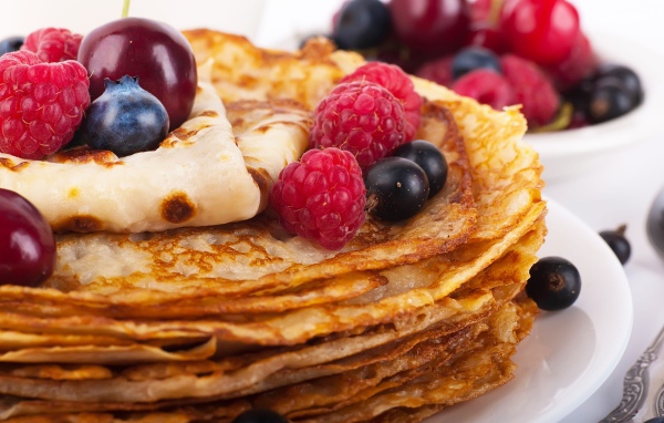 Блины с ягодами черники и малины на белой тарелке 