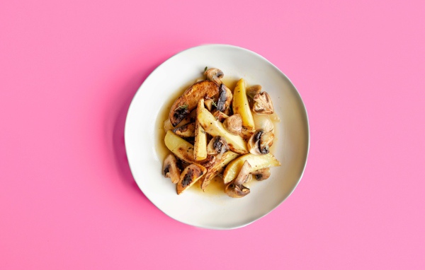 Картофель с грибами в тарелке на розовом фоне 