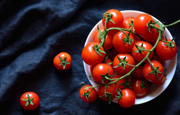 Красные помидоры в белой миске на черном фоне