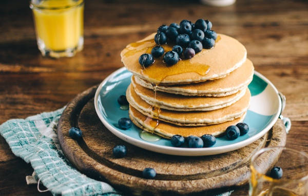 Румяные оладья на тарелке  с медом и ягодами черники 