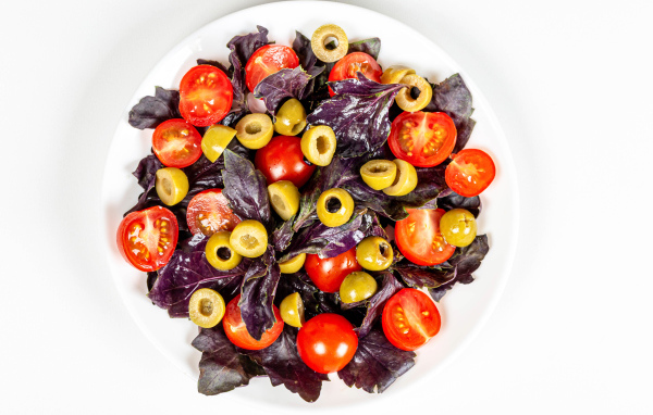 Салат с листьями базилика, помидорами и оливками на белом фоне