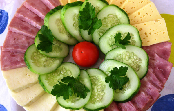 Сыр нарезанный, огурцы и ветчина на тарелке 