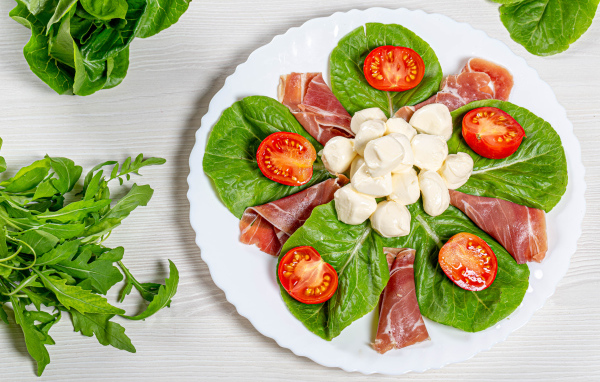 Кусочки ветчины на тарелке с сыром, помидорами и листьями салата