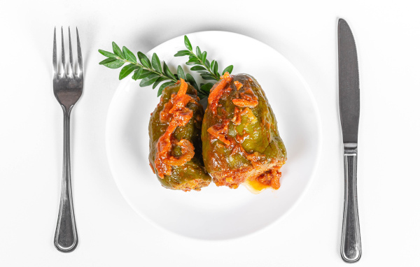 Фаршированный перец на белой тарелке со столовыми приборами