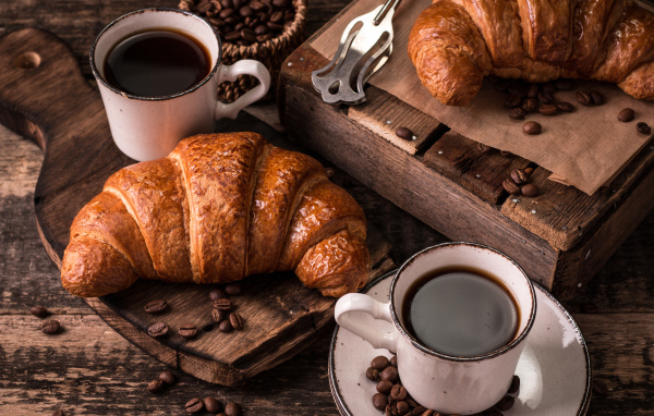 Две чашки кофе на столе с рогаликами и зернами 