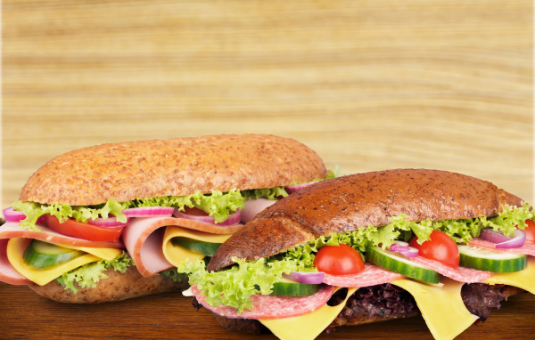 Два аппетитных сэндвича с колбасой и овощами на столе