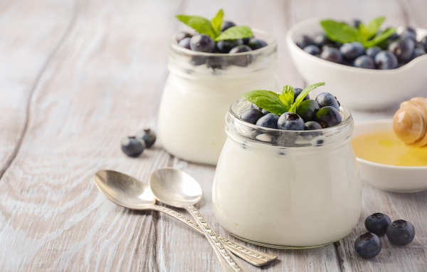 Йогурт в банках с ягодами черники на столе с ложками и медом