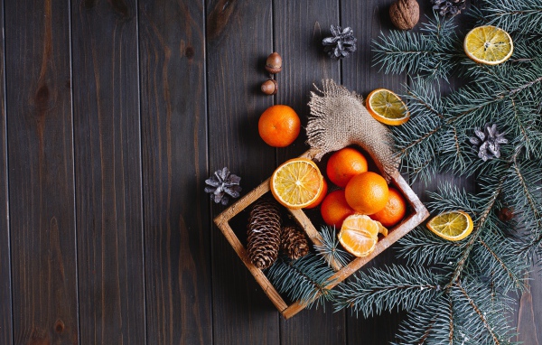 Ящик с мандаринами и шишками на столе с еловыми ветками