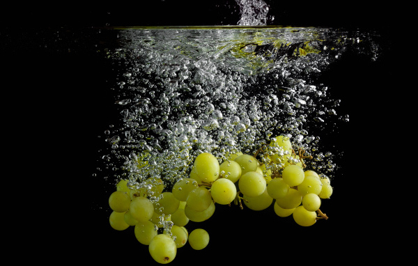 Ягоды белого винограда в воде на черном фоне
