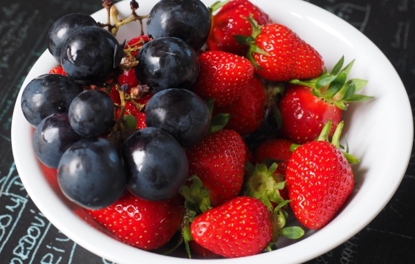 Синий виноград на тарелке с ягодами клубники 