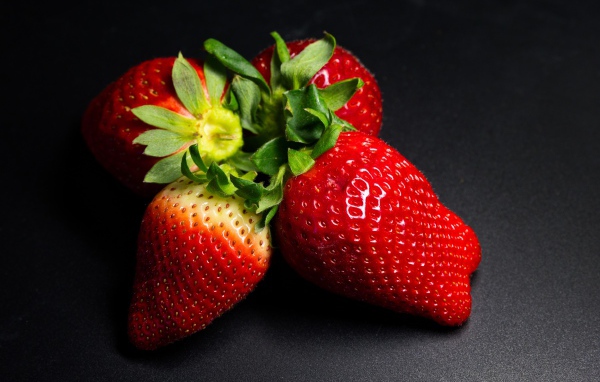 Четыре спелых красных ягоды клубники на черном столе 